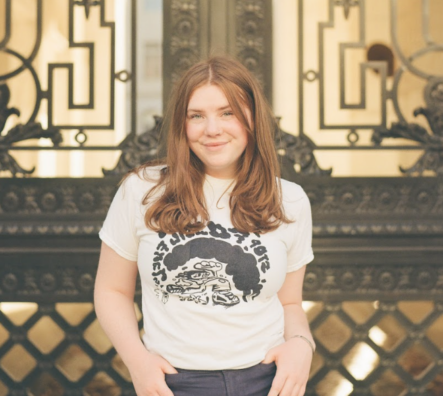 Ella Weber stands smiling in front of large doors.