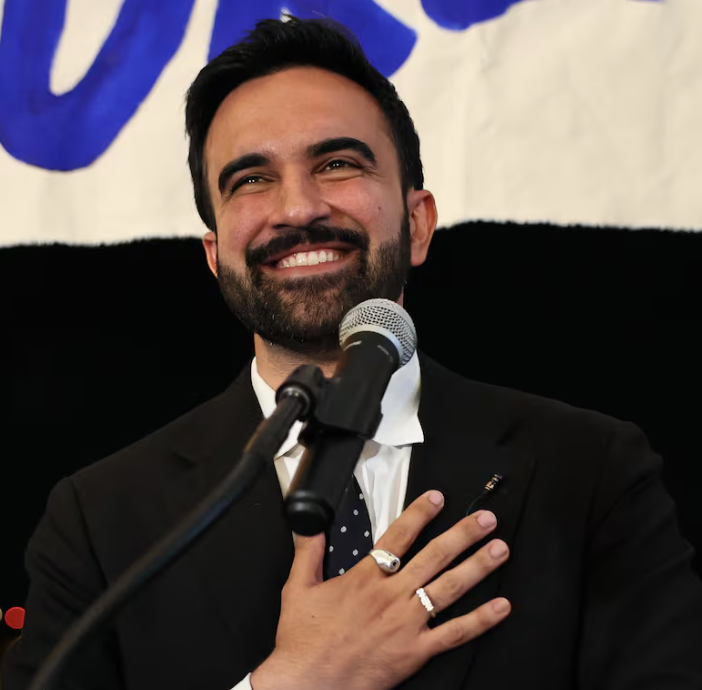 Zohran Mamdani smiles at a microphone on his primary election night.